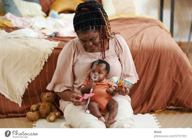 Black woman sitting on floor and playing with baby girl sucking pacifier toy mother kid soother leisure newborn motherhood little sleep calm give child care
