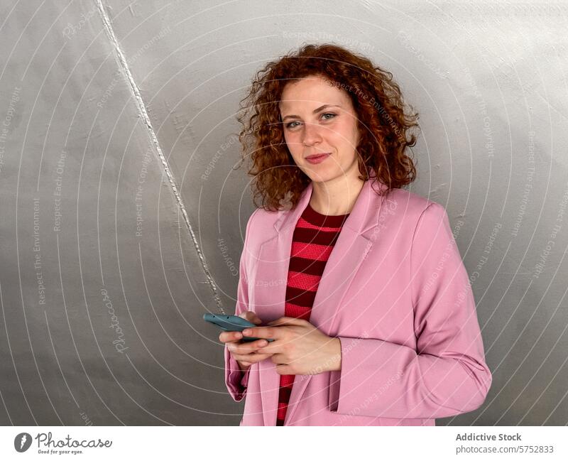 Rothaarige Frau mit Mobiltelefon vor grauem Hintergrund Smartphone Geschäftsfrau krause Haare selbstbewusst Stehen grauer Hintergrund Beteiligung Handy