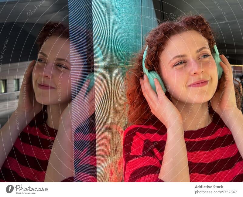 Junge rothaarige Frau genießt Musik mit Kopfhörern im Freien jung Lächeln krause Haare rote Haare Reflexion & Spiegelung Glas blaugrün gestreiftes Hemd Genuss