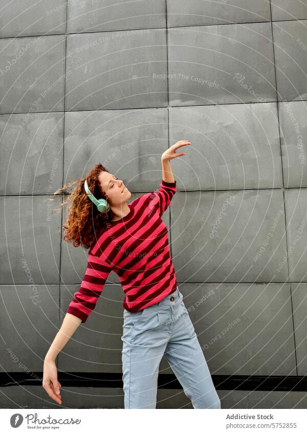 Junge rothaarige Frau in gestreiftem Hemd genießt die Musik im Freien jung Kopfhörer Tanzen urban Wand grau sorgenfrei Rhythmus Favorit Gesang Genuss Freizeit