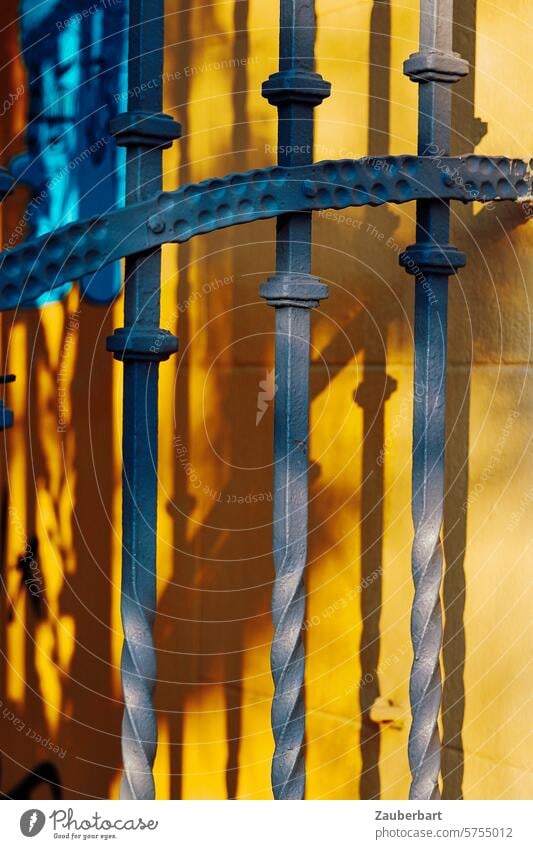 Schmiedeeisernes Tor wirft Schatten auf gelbe Wand, Detailaufnahme geschmiedet eisen schmiedeeisern Schattenwurf Eisen alt historisch Metall Tür Eingang