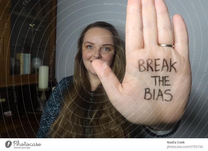Junge Frau im Hintergrund hält die Hand im Vordergrund hoch, auf deren Handfläche "Break the Bias" geschrieben steht das Vorurteil zu brechen Handschrift Rechte