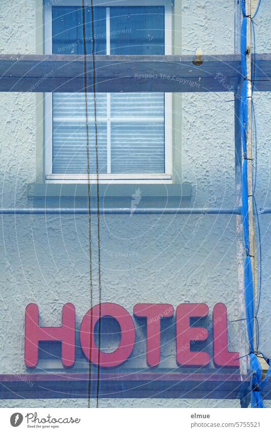 roter Schriftzug HOTEL an einem Gebäude hinter einem blauen Gerüstnetz Hotel Baustelle Baugerüst Stoppnetz Baustelleneinrichtung Personenauffangnetz