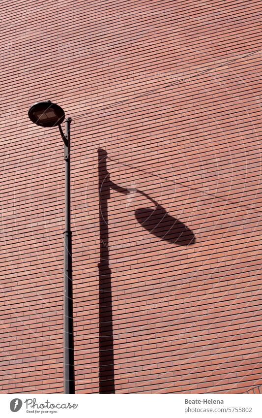 Beleuchtete Leuchte in  Paris Straßenbeleuchtung Schatten Backsteinwand Wand Mauer Außenaufnahme Menschenleer Fassade Strukturen & Formen Architektur