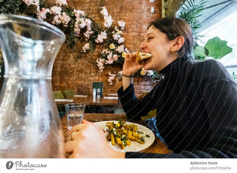 In einem Moment der Freude beißt eine Frau in ein Sandwich, umgeben von einer einladenden Café-Atmosphäre mit lebhaftem Blumendekor an der Wand Belegtes Brot