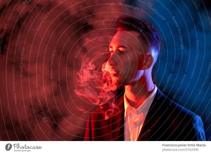 Eleganter junger Mann, der Zigarettenrauch aus seinem Mund bläst, auf schwarzem Hintergrund. Selektiver Fokus Rauch Geschäftsmann Zigarre Gesundheit Anzug