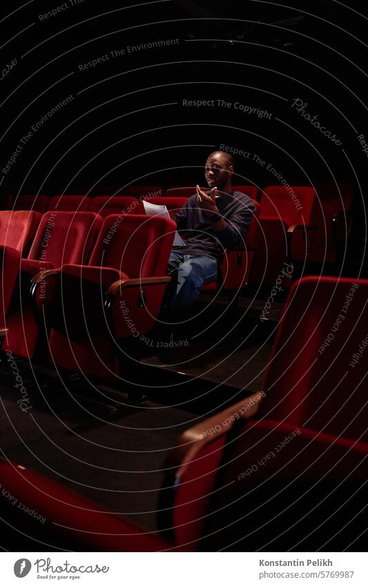 Vertikale Aufnahme eines afroamerikanischen Mannes, der im Publikum sitzt und vor der Vorstellung im leeren Theater den Text liest Künstler Künstlerin