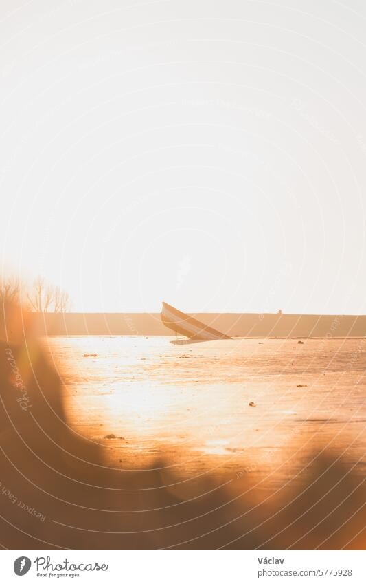 Ein sinkendes Schiff im Treibsand bei Sonnenaufgang an der Küste der Niederlande. Letzte Fetzen von Hoffnung und Leben. Orangefarbenes Leuchten und das sinkende Schiff
