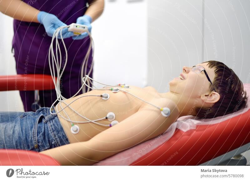 Kind unter EKG-Test mit Arzt. Junge Patient liegt in medizinischen Bett mit Vakuum-Sensoren. Eine Krankenschwester führt ein Elektrokardiogramm des Herzens im Büro einer medizinischen Klinik durch. Untersuchung des Herzens