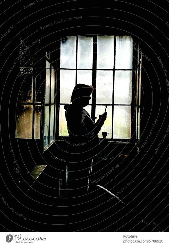 Da steht sie in einem von Ruß geschwärzten Raum und macht mit dem Handy ein Foto im Gegenlicht vor einem Fenster schwarz Frau Silhouette Schatten Licht Kontrast