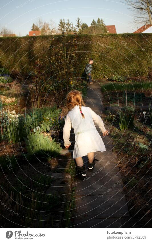 zwei Kinder spielen Fangen im Garten fangen Fröhlichkeit Freude Glück Spaß Mädchen Junge Kleid Zöpfe Kinderspiel kindlich Spielregel miteinander toben jagen