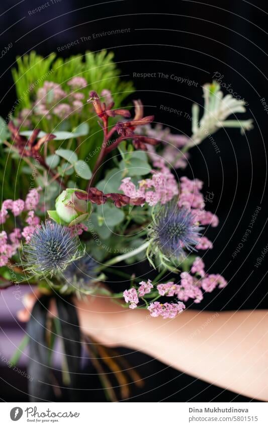 Blumenstrauß-Arrangement mit exotischer Eryngium-Blüte und grüner Koniferenpflanze auf vertikalem schwarzen Hintergrund mit Kopierraum Dekoration & Verzierung