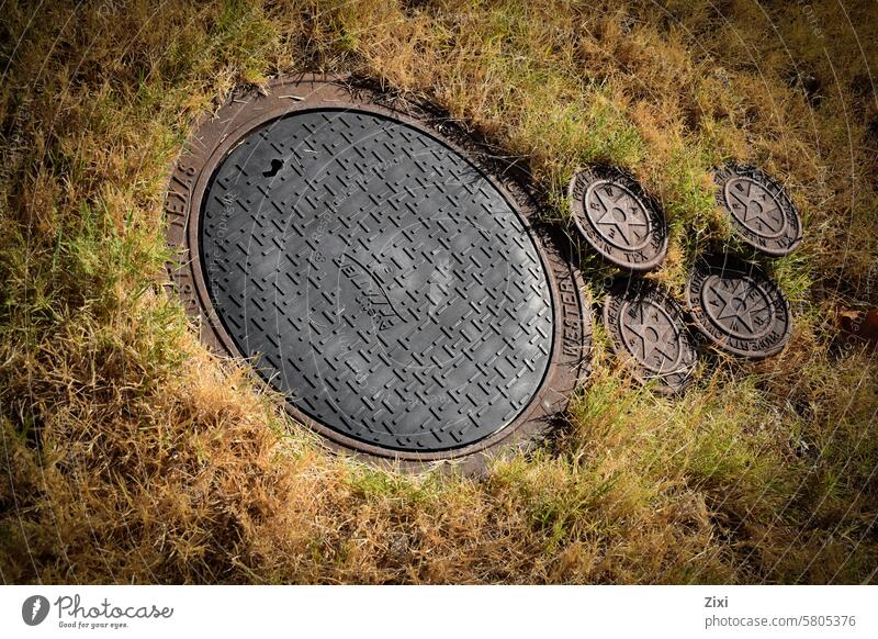 Große und kleine Kanalisationsdeckel Kanalloch Abwasserkanal groß und klein Gras