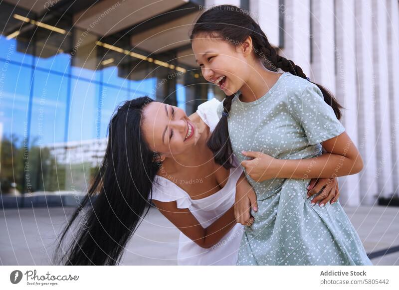 Umarmung zwischen Mutter und Tochter mit Autismus-Spektrum Lachen Zusammensein freudig Umarmen spielerisch Liebe modern Gebäude im Freien Fröhlichkeit Familie