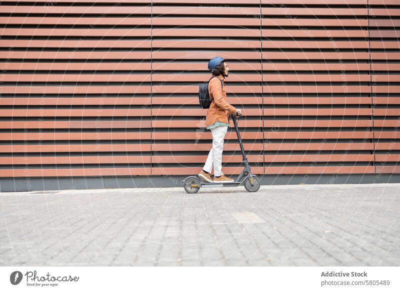 Urbaner Lebensstil: junger Mann auf einem Elektroroller urban umweltfreundlich Verkehr Vollbart Schutzhelm blau modern gestreifter Hintergrund Lifestyle