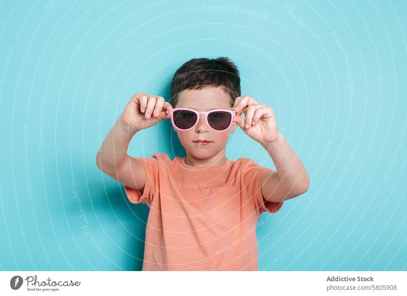 Junger Junge mit Sonnenbrille auf türkisem Hintergrund Kind Schule Jugend cool Stil selbstbewusst starren Fotokamera Porträt Mode Accessoire Persönlichkeit