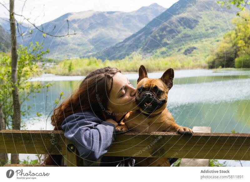 Weiblicher Reisender küsst Hund in der Nähe eines Sees in den Bergen Frau Kuss Berge u. Gebirge französische Bulldogge Freund reisen Zusammensein Pyrenäen Natur