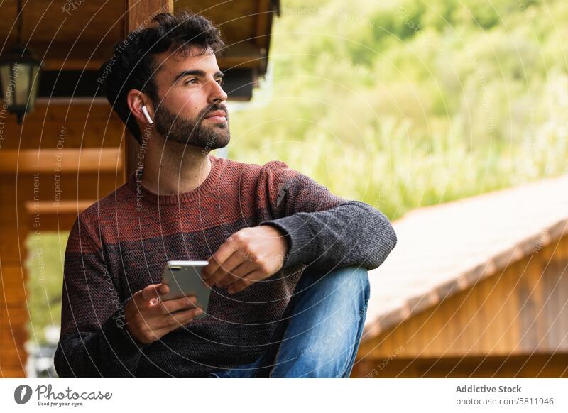 Nachdenklicher Mann, der auf einer Terrasse mit Ohrstöpseln Musik hört zuhören Smartphone benutzend echte drahtlose genießen Gesang männlich Pyrenäen Kopfhörer