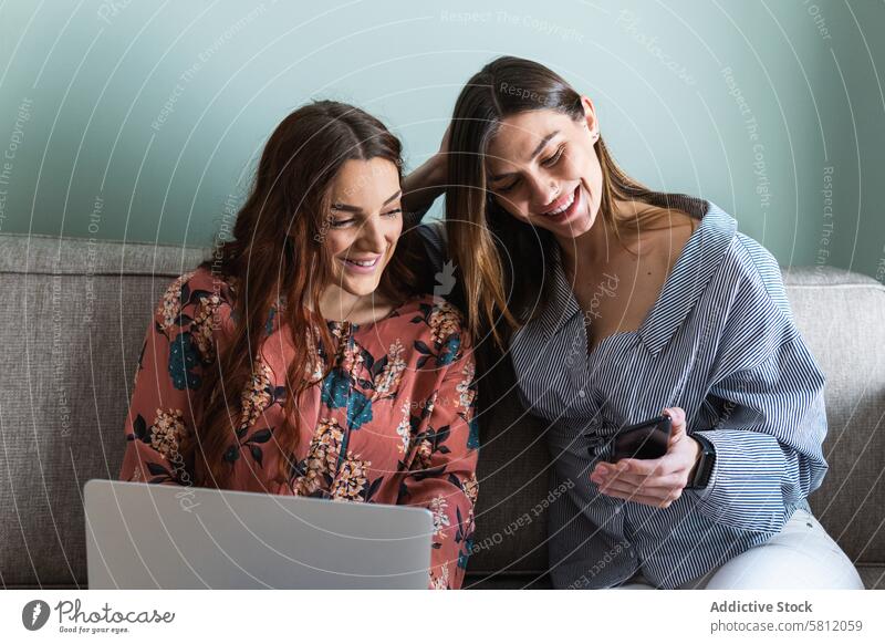 Junge Frauen ruhen sich auf dem Sofa aus und surfen auf ihren Smartphones benutzend Zusammensein Windstille Komfort Browsen Freund Apparatur Wohnzimmer Kälte