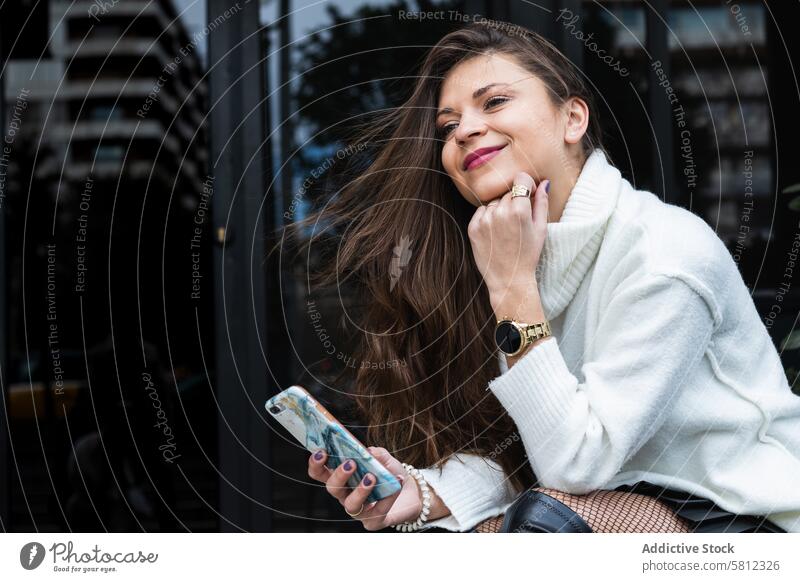 Glückliche stilvolle Frau mit Smartphone und Armbanduhr Stil träumen Telefon trendy Accessoire urban gestrickt Pullover Erwachsener Mobile Apparatur Gerät