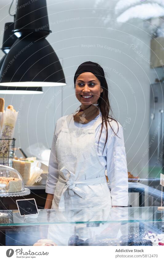 Fröhliche Frau am Tresen einer Bäckerei Abfertigungsschalter Vitrine Lächeln Gastfreundschaft Verkaufswagen Personal Arbeit Uniform professionell Job Dessert