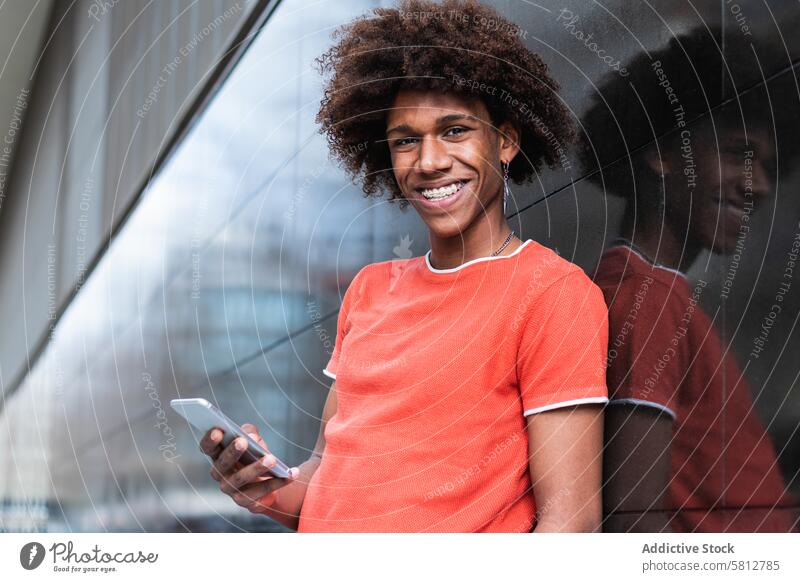 Erfreuter junger ethnischer Mann, der sein Smartphone benutzt und auf der Straße lächelt Nachricht Lächeln Inhalt Stil Internet Kommunizieren online heiter
