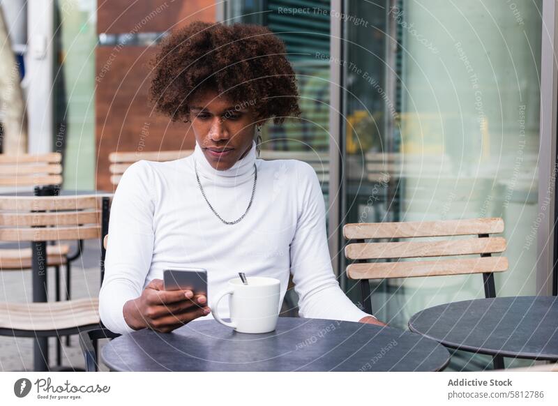 Seriöser junger ethnischer Mann benutzt Smartphone in einem Straßencafé Nachricht Café Kaffeepause Selbstwertgefühl Kommunizieren online Kälte soziale Netzwerke