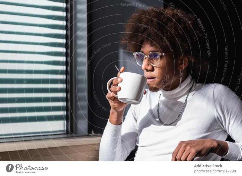 Nachdenklicher junger ethnischer Mann trinkt Kaffee und schaut in einem Café weg trinken sich[Akk] entspannen besinnlich Kaffeepause Kälte Stil genießen