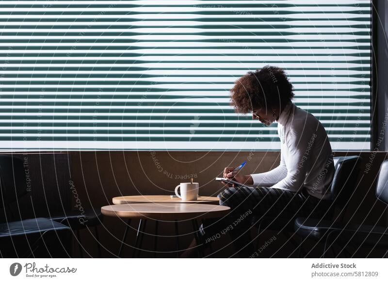 Konzentrierter junger Schwarzer, der sich Notizen macht, während er in einem Café mit einer Tasse Kaffee chillt Mann zur Kenntnis nehmen Schüler Konzentration