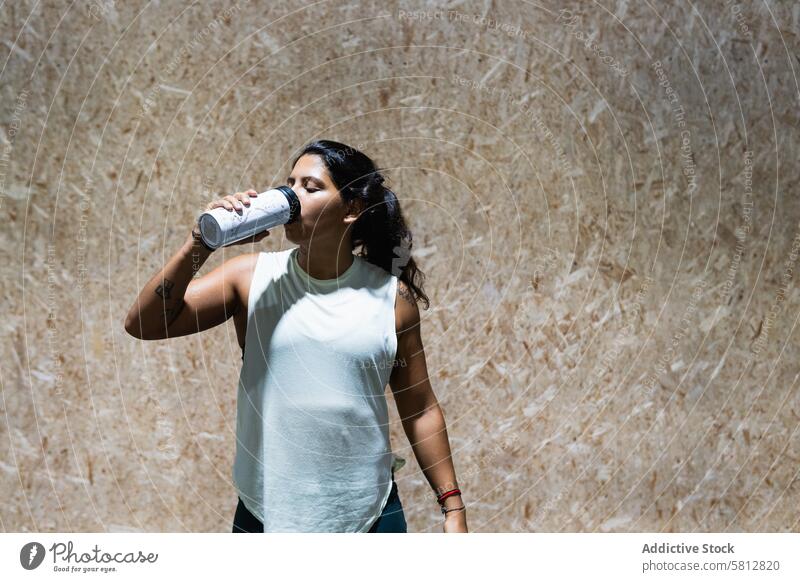 Hispanische Frau trinkt Wasser im Fitnessstudio Sportlerin trinken Hydrat Training Wellness Gesunder Lebensstil muskulös selbstbewusst Durst Flasche sportlich