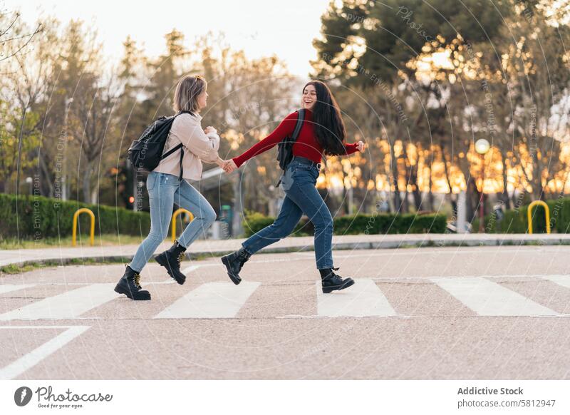 zwei Studentinnen überqueren den Zebrastreifen, halten sich an den Händen, laufen und lächeln Straße Mädchen Menschen Großstadt Verkehr Spaziergang urban Kind