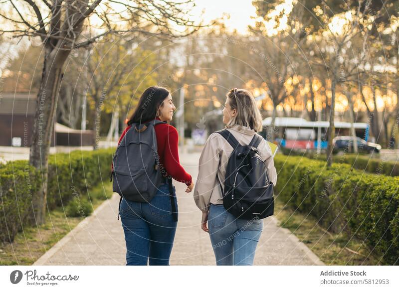 Rückenansicht von zwei Studentinnen, die auf dem Campus spazieren gehen und sich unterhalten Freundschaft Zusammensein außerhalb jung Glück Freunde