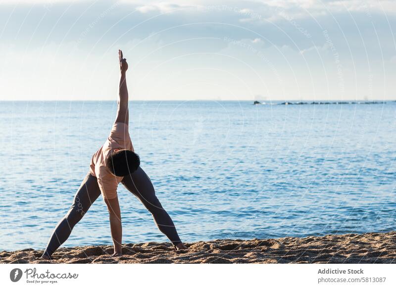 Flexibler Mann bei einer verdrehten Yoga-Asana am Meer Strand gedrehte weitbeinige Vorwärtsbeuge verdrehen Pose üben stehen Gleichgewicht männlich Lifestyle