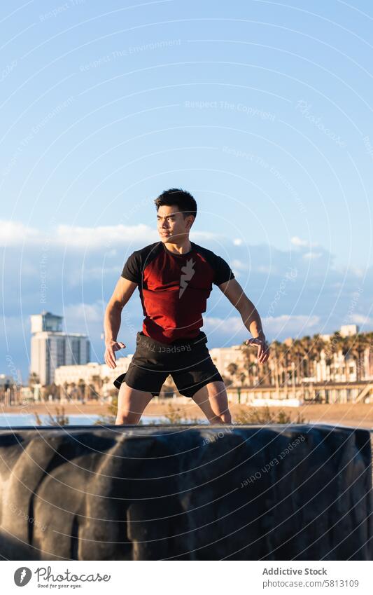 Starker ethnischer Sportler, der während des Fitnesstrainings in der Nähe des Reifens springt Training Übung springen stark Energie sportlich Aufwärmen Mann