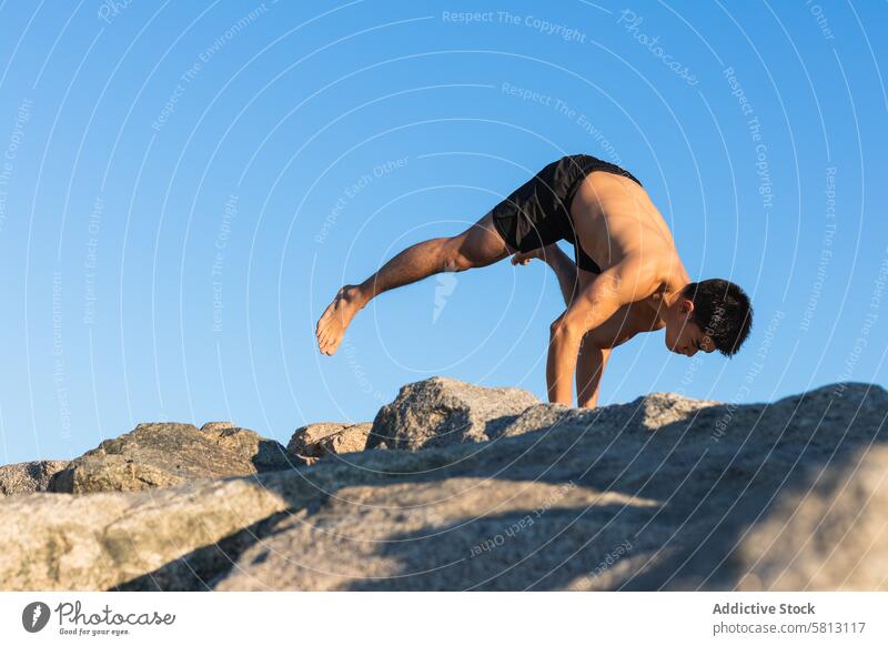 Ethnischer Mann macht Arm Balance Yoga-Pose auf Stein Gleichgewicht Asana fliegende Taube eka pada galavasana fortgeschritten üben Handstand männlich ohne Hemd