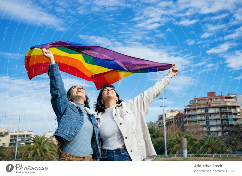 Mit der Pride-Flagge unter blauem Himmel die Vielfalt zelebrieren Stolz Fahne lgbtq+ Freunde Feier Freude Blauer Himmel Freiheit Gemeinschaft abstützen