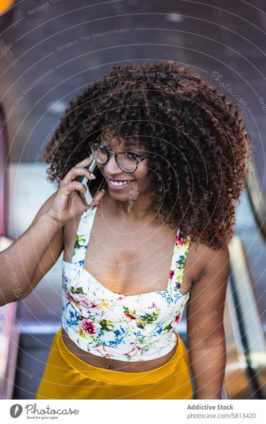 Freudige afroamerikanische Frau, die im Park über ihr Smartphone spricht sprechen Lächeln Sommer Stil Glück krause Haare Brille Telefon Anruf reden heiter