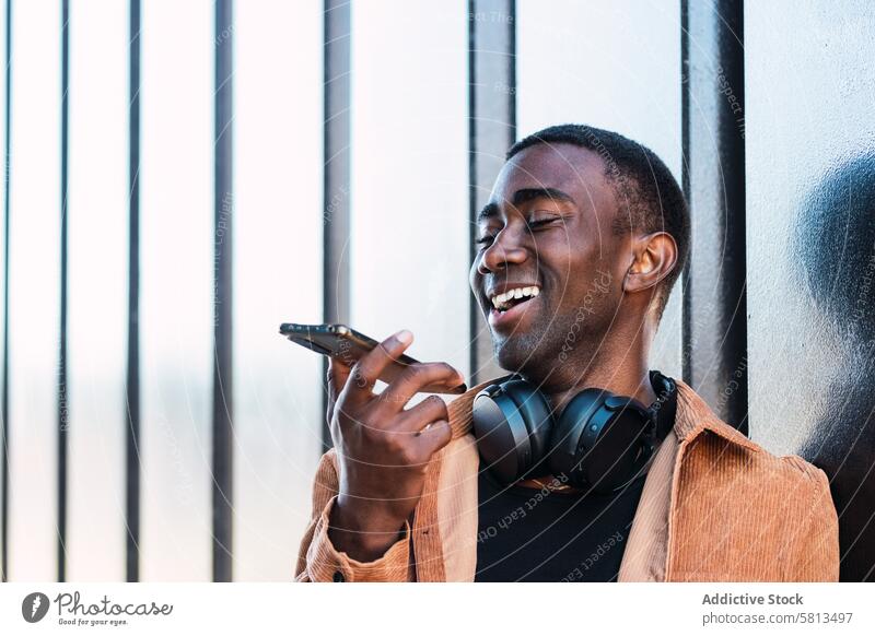Schwarzer Mann mit Kopfhörern, der eine Sprachnachricht aufnimmt Smartphone Stimme Nachricht Audio meloman Wand Straße Aufzeichnen Großstadt benutzend Anschluss