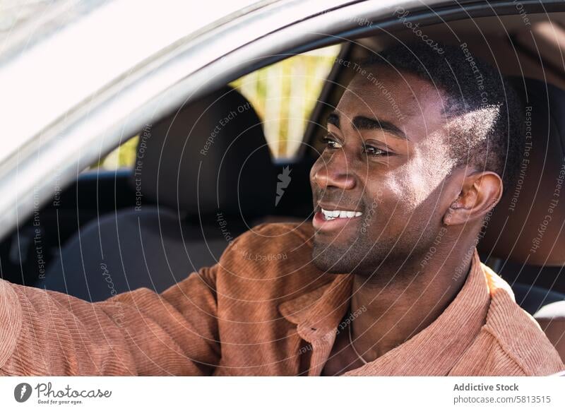 Fröhlicher schwarzer Mann im Auto PKW Fahrer Automobil Laufwerk Lächeln Arbeitsweg Vorschein Fenster Straße Lenkrad positiv Afroamerikaner Verkehr modern