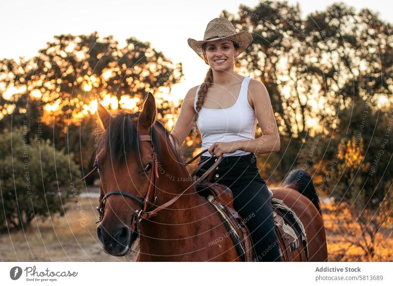 Junge Frau mit Hut reitet auf einem Pferd in der Landschaft bei Sonnenuntergang Natur jung Tier Ranch Cowgirl Cowboy Person pferdeähnlich Reiten schön Reiterin