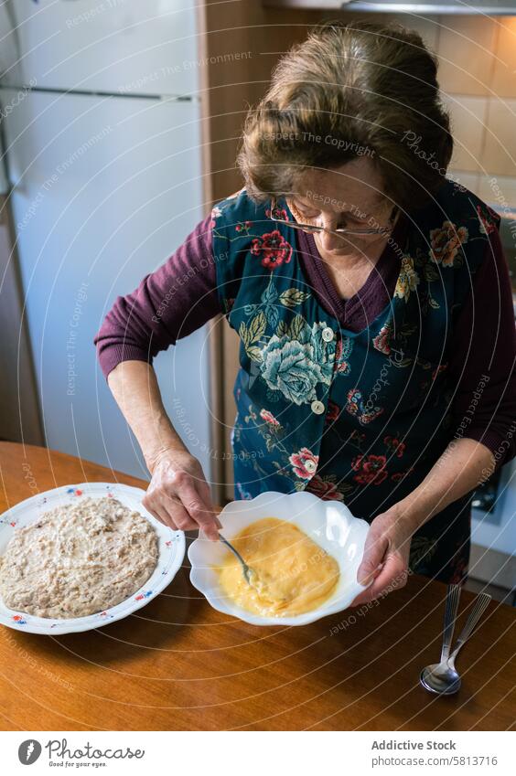 Ältere Frau schlägt zu Hause Eier auf und macht handgemachte Kroketten vertikal gealtert schlagend heimwärts handgefertigt mischen Keramik stehen Geduld Liebe