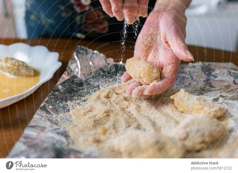 Ältere Frau bestreicht Kroketten zu Hause mit Paniermehl Nahaufnahme gealtert Hände Senior Belag Brotkrümel heimwärts Vorbereitung Küche selbstgemacht