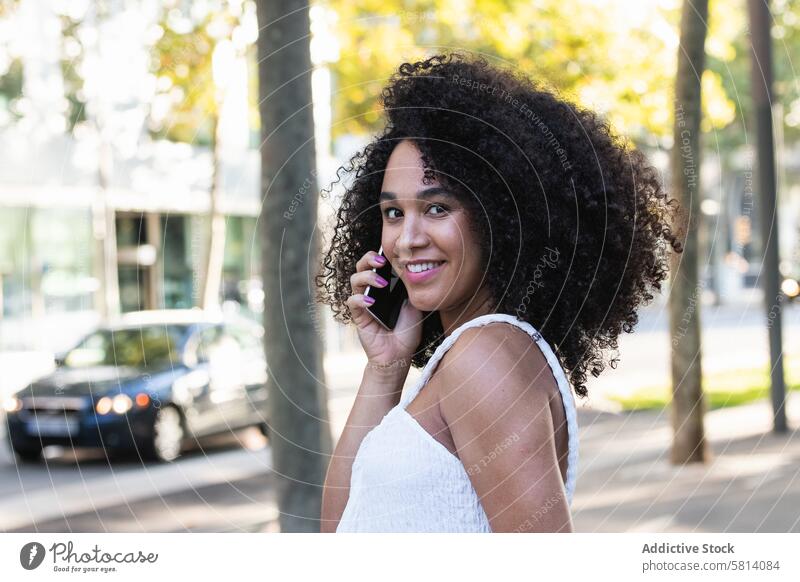 Lächelnde schwarze Frau beim Telefonieren mit dem Smartphone benutzend Anschluss sprechen positiv Mobile online Gerät Afro-Look Funktelefon Frisur sorgenfrei