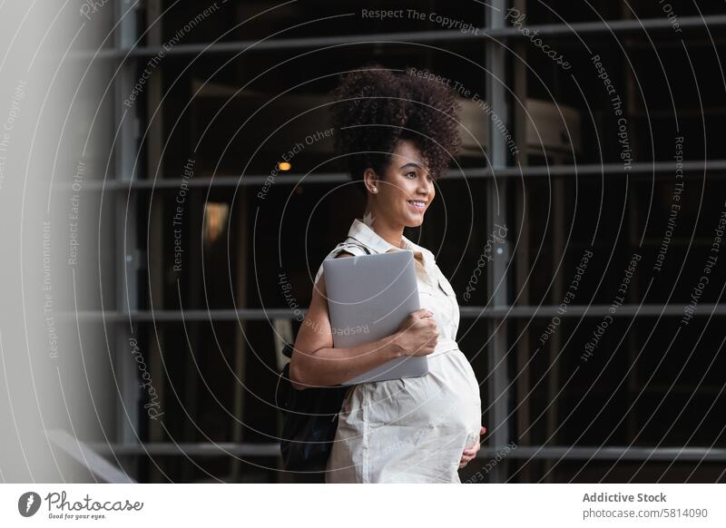 Lächelnde schwarze Frau mit Laptop kommt aus einem Bürogebäude schwanger führen mütterlich vorwegnehmen erwarten Turm Glück Bauch Apparatur Gerät digital Freude