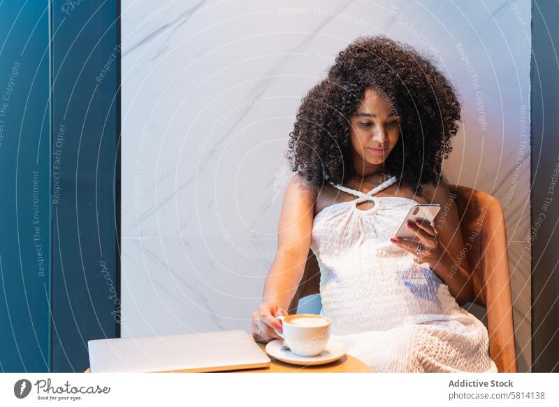 Schwarze Frau, die mit einer Tasse Milchkaffee auf ihrem Smartphone surft benutzend schwanger positiv Kaffee Latte Browsen Funktelefon Apparatur Mobile