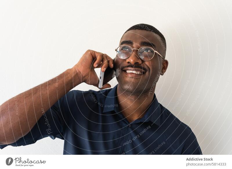 Schwarzer Mann mit Telefon in der Nähe der weißen Wand Smartphone gut gekleidet modern Lächeln Glück froh Brille Studioaufnahme Netbook schwarz Afroamerikaner