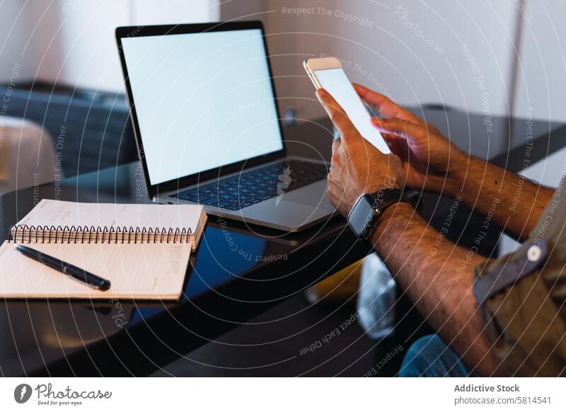 Anonymer Mann durchsucht Smartphone in der Nähe des Laptops Browsen online Internet Arbeit Arbeitsplatz modern leerer Bildschirm Textnachricht abgelegen