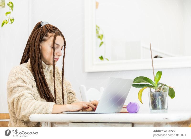 Nachdenkliche Frau mit Dreadlocks, die zu Hause mit einem Laptop arbeitet heimwärts Computer Sitzen Raum Internet Technik & Technologie Menschen Lifestyle jung