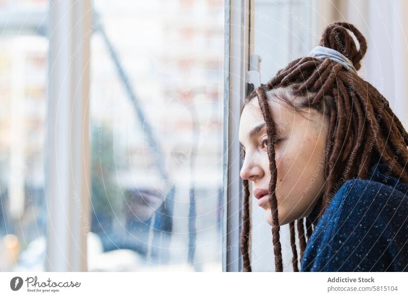 Nachdenkliche Frau mit Dreadlocks schaut aus dem Fenster besinnlich heimwärts Blick Menschen Denken Rastalocken Zopf Kontemplation schön Porträt Person