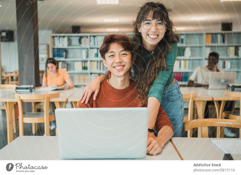 Fröhliche Studenten mit Laptop in der Bibliothek Schüler Freund Lächeln lernen Universität Zusammensein Porträt Umarmung Bildung Teenager jung Jugendlicher